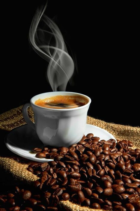 A cup of coffee with smoke on a saucer and beans
